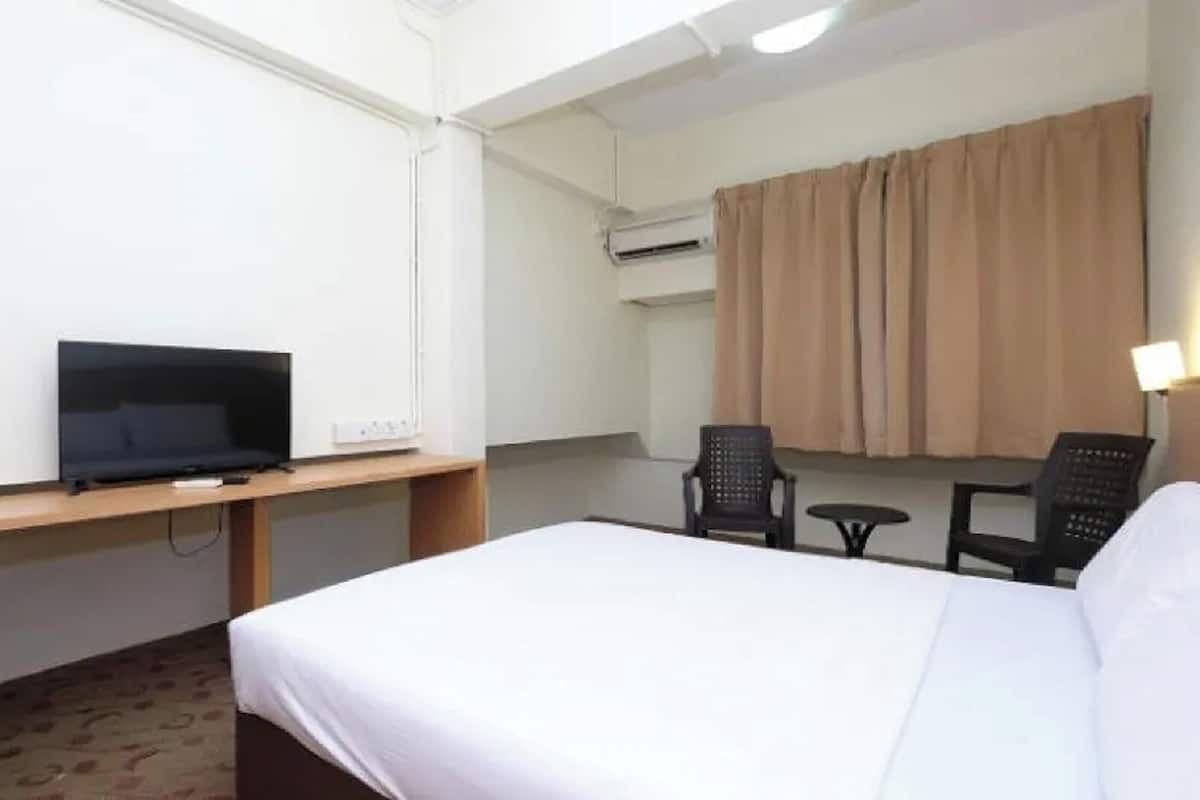 Una habitación de hotel con cama, escritorio con televisor, silla, una mesita y aire acondicionado.