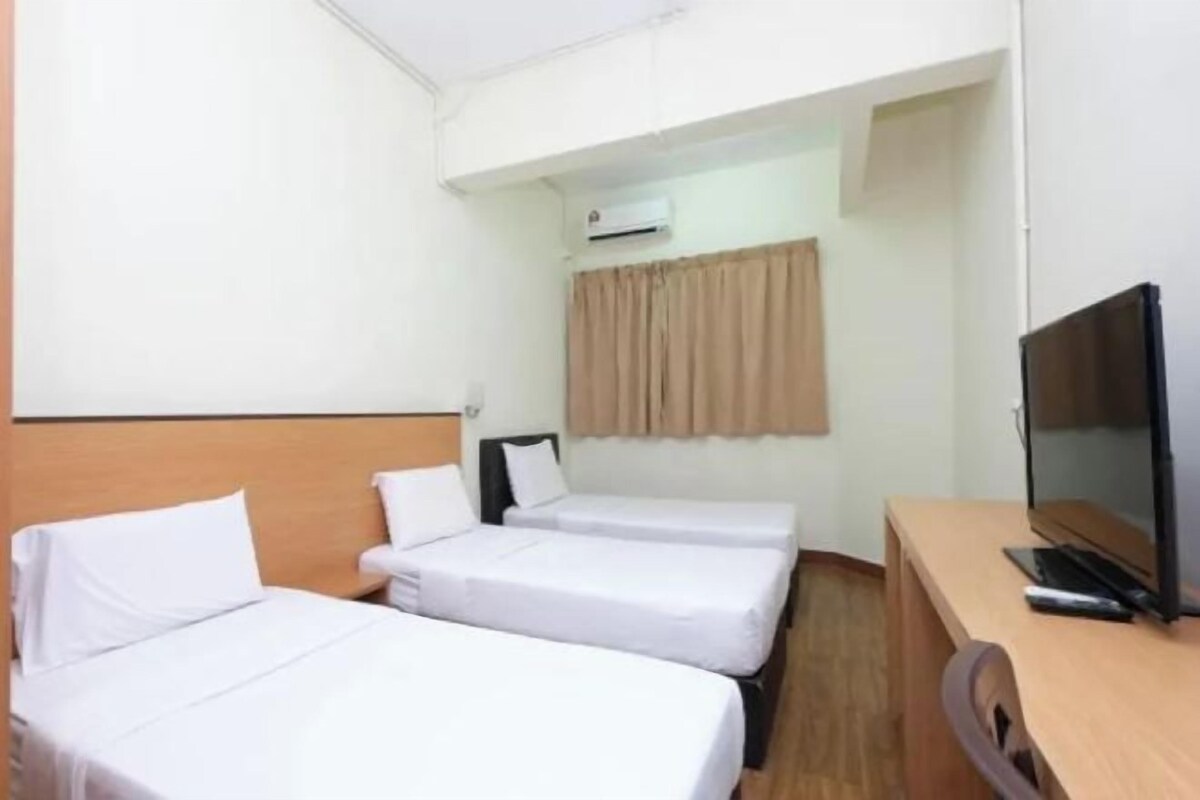 A hotel room with two single beds, a desk with a television, and an air conditioning unit.