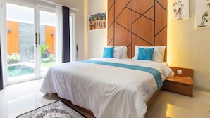 A bedroom with a large bed, a wooden headboard, and a view of a garden through glass doors. - Kamboja Villa By Zuzu (Kerobokan)