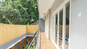 A modern balcony with a wooden railing, a stone wall, and a glass door leading to a pool area. - Kamboja Villa By Zuzu (Kerobokan)