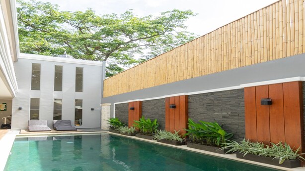 A modern pool area with a clear pool, wooden deck, and potted plants. - Kamboja Villa By Zuzu (Kerobokan)