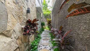 A narrow stone pathway flanked by lush plants and a stone wall. - Kamboja Villa By Zuzu (Kerobokan)