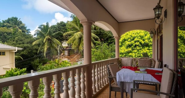 A balcony with a table and chairs, overlooking a lush garden and a building.