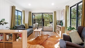 Un salon moderne avec un plancher en bois, un canapé, une table basse et une grande porte vitrée donnant sur une terrasse extérieure.