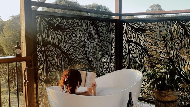 Un bain à remous extérieur moderne, doté d’une terrasse en bois et d’un mur décoratif orné d’un motif de feuilles.