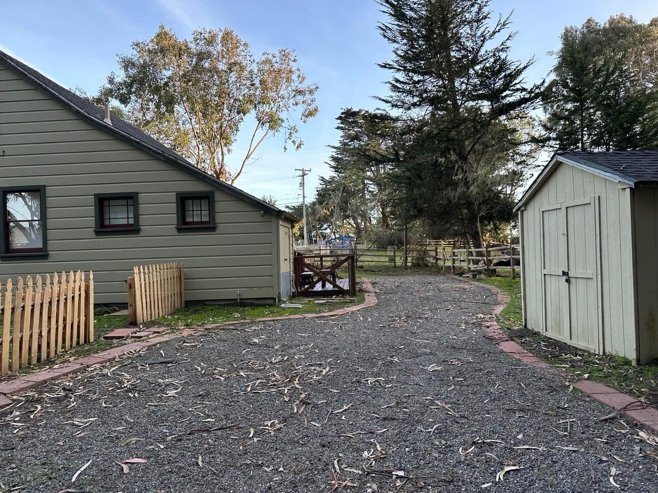 A gravel driveway leading to a building with a wooden fence and a shed.