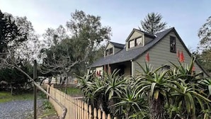 A two-story house with a wooden fence and tropical plants in front. - Harbor Kee Peaceful Escape By The Bay (Bodega Bay)