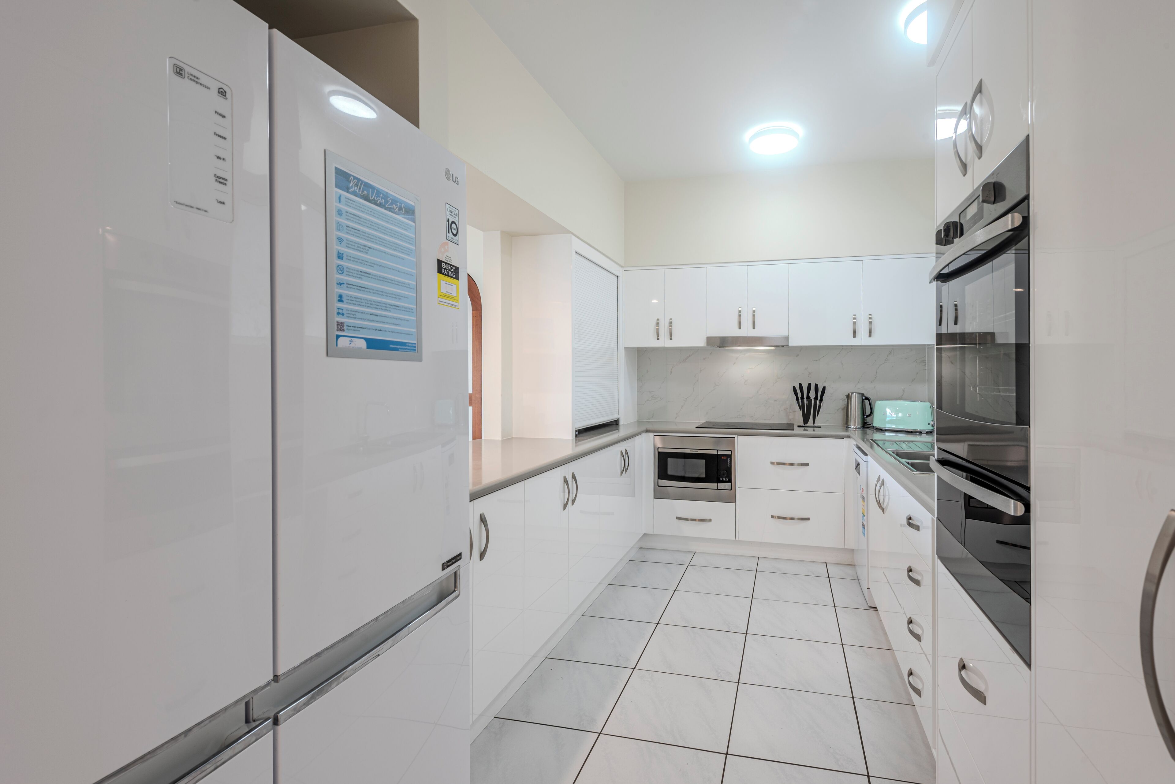 A modern kitchen with white cabinets, stainless steel appliances, and a tiled floor.