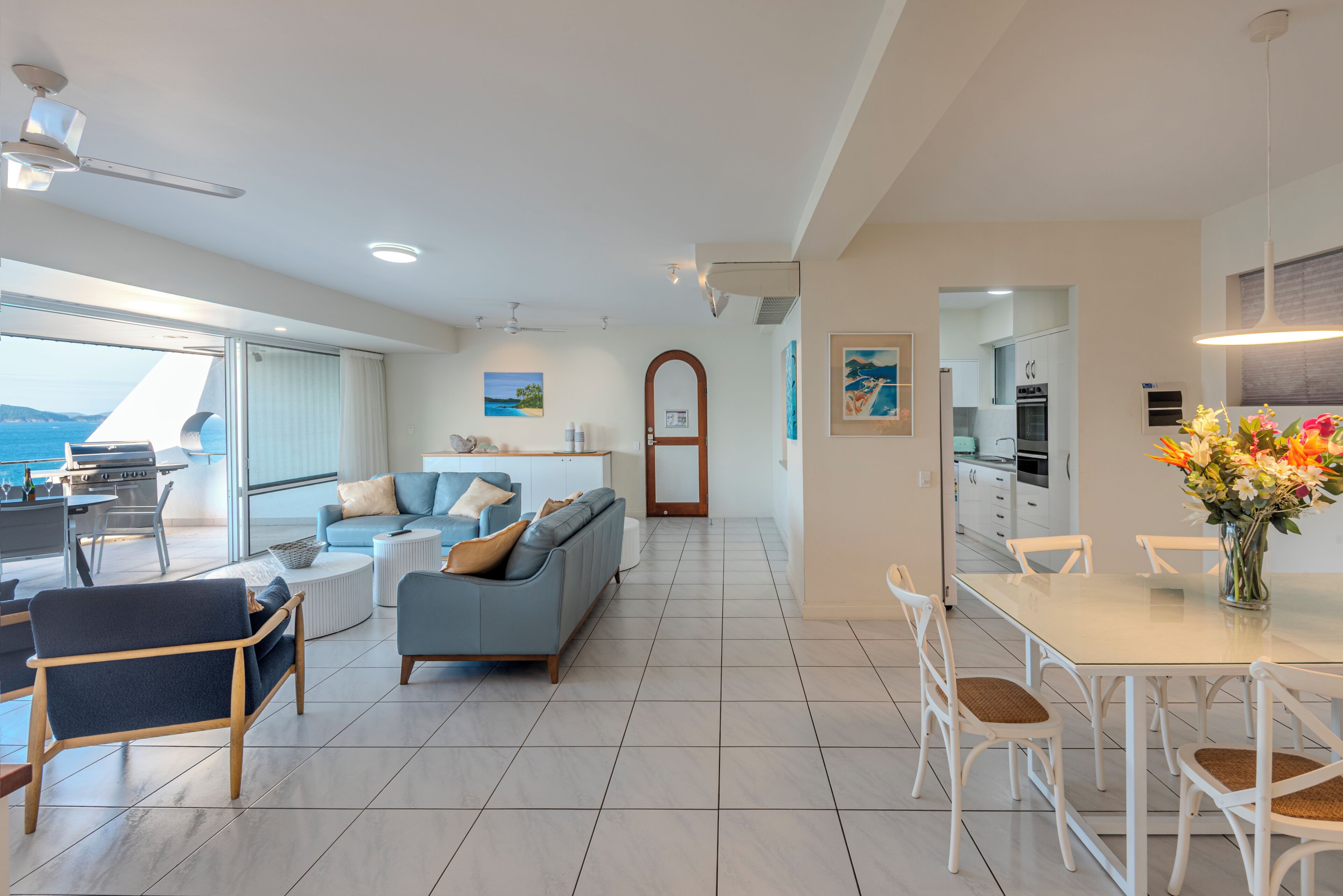 A modern living room with a sofa, chairs, and a dining table. There is a kitchen area with cabinets and a dining table.