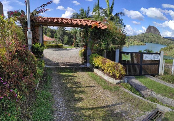 A paved pathway leading to a gated entrance with a red-tiled roof structure overhead. - Casa de Campo Con Vista a la Piedra (El Peñol)