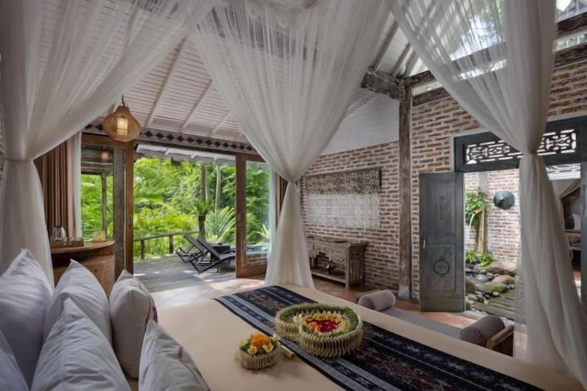 Une chambre avec un lit, une table agrémentée d’un élément décoratif, un balcon avec une chaise et un mur en briques.