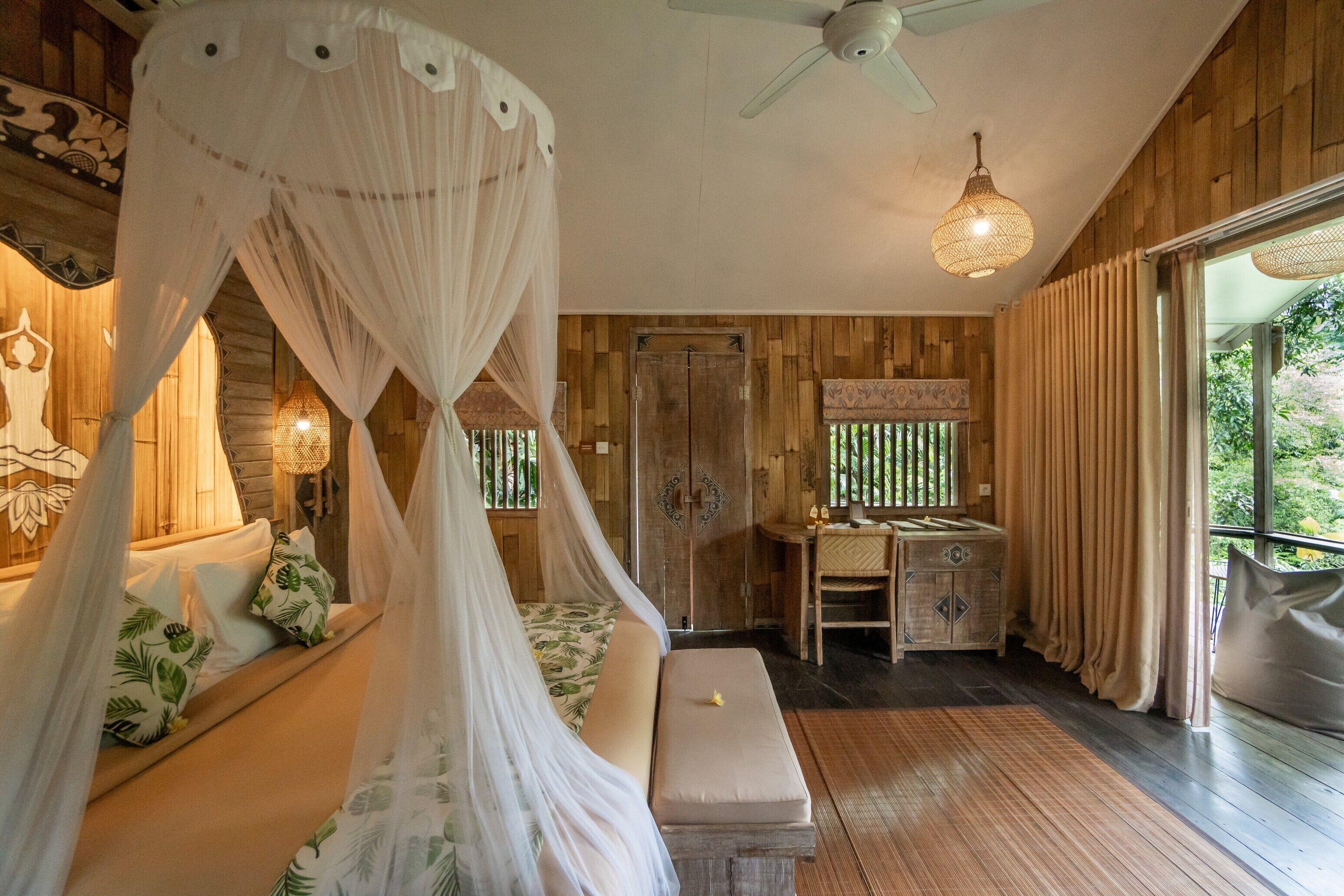 Une chambre dotée d’un lit à baldaquin, de murs en bois, d’un ventilateur de plafond, d’un bureau avec une chaise et d’une grande fenêtre.