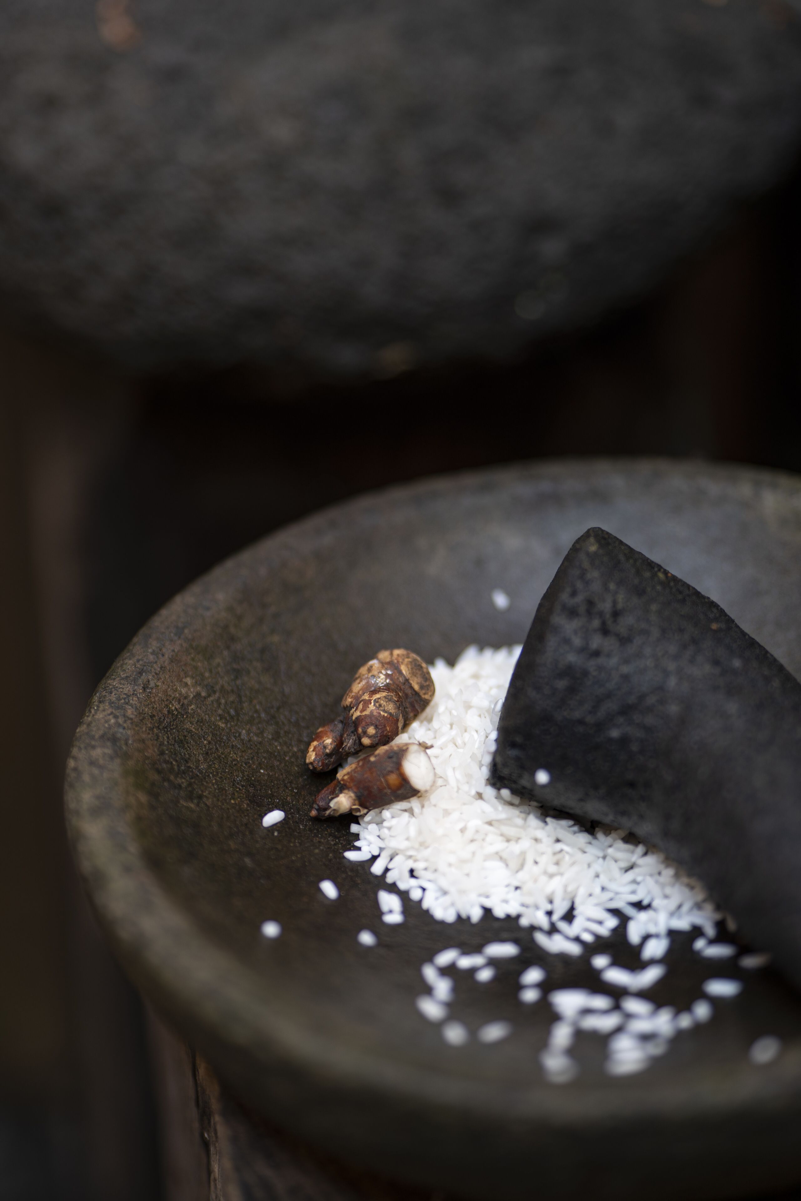 Un mortero de piedra con arroz blanco y un objeto marrón, posiblemente una especia, sobre una superficie de madera.