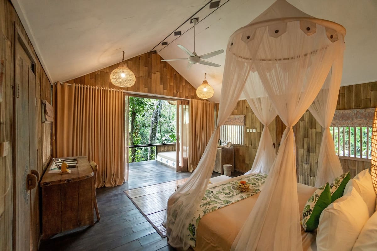 Une chambre à coucher avec un lit à baldaquin, des murs en bois, un ventilateur de plafond et une vue sur l’extérieur.