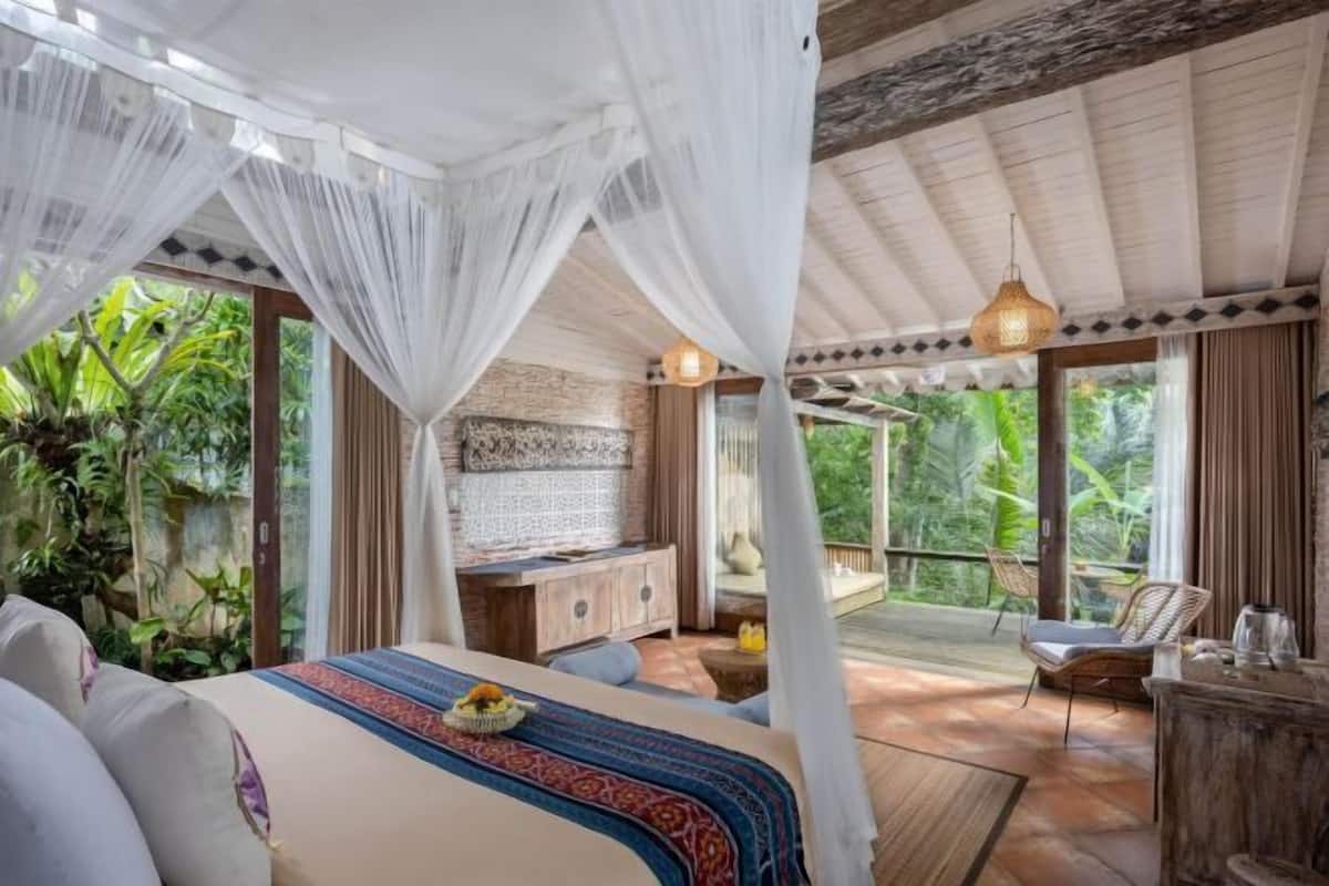 Une chambre avec un lit, une petite table, une chaise et un balcon donnant sur un paysage verdoyant.