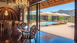 A spacious indoor area with a pool, lounge chairs, and a glass-enclosed patio with a view of mountains. - Mont Eco Game Reserve (Montagu)