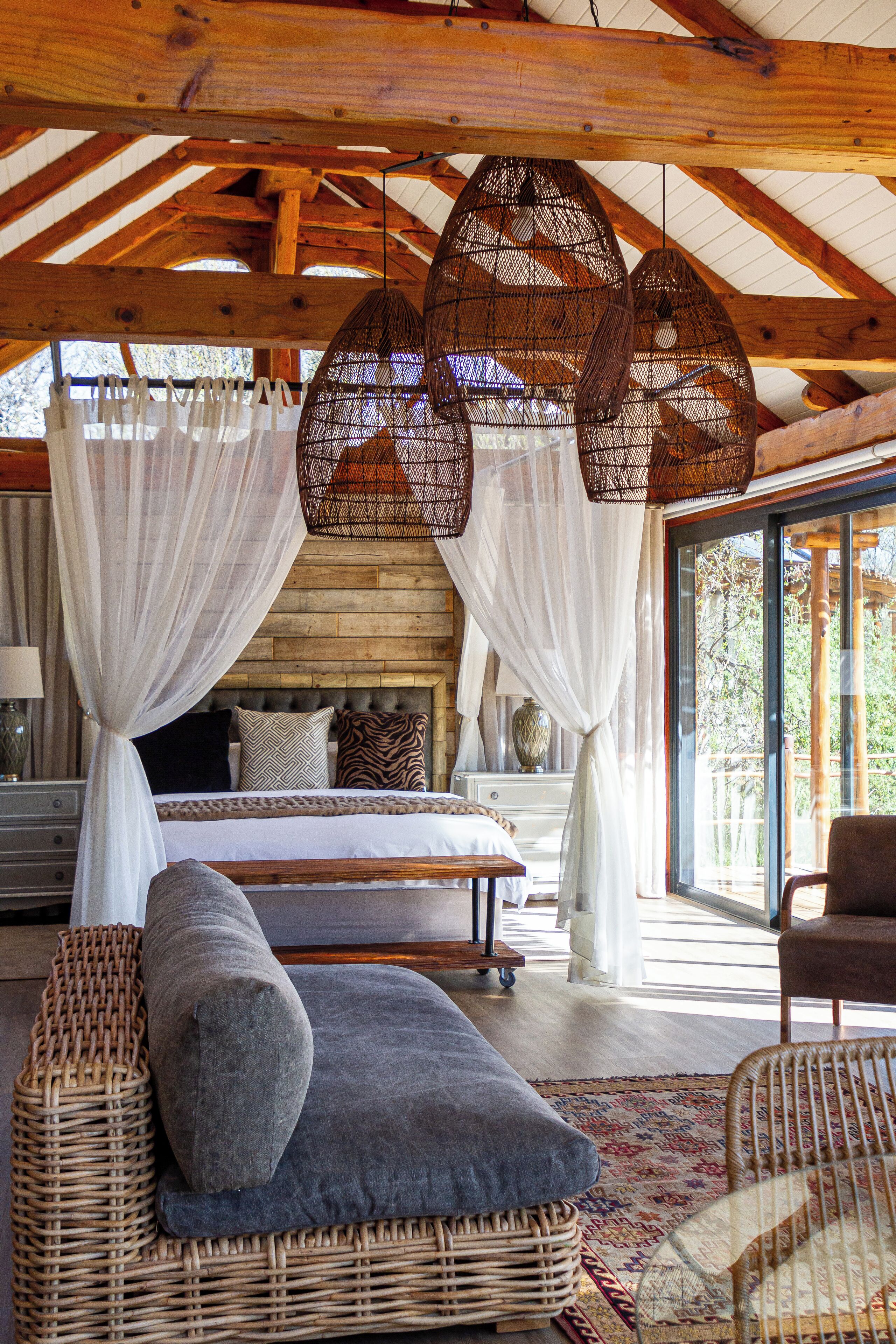A spacious bedroom with a large bed, a wicker sofa, and a wicker chair. There are two hanging wicker lamps above the bed. - Mont Eco Game Reserve (Montagu)