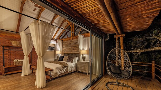 A bedroom with a wooden ceiling, a bed with white bedding, a hanging chair, and a view of the outdoors. - Mont Eco Game Reserve (Montagu)
