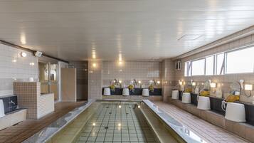 Um banheiro moderno com piscina central, vários lavatórios com espelhos e piso ladrilhado.