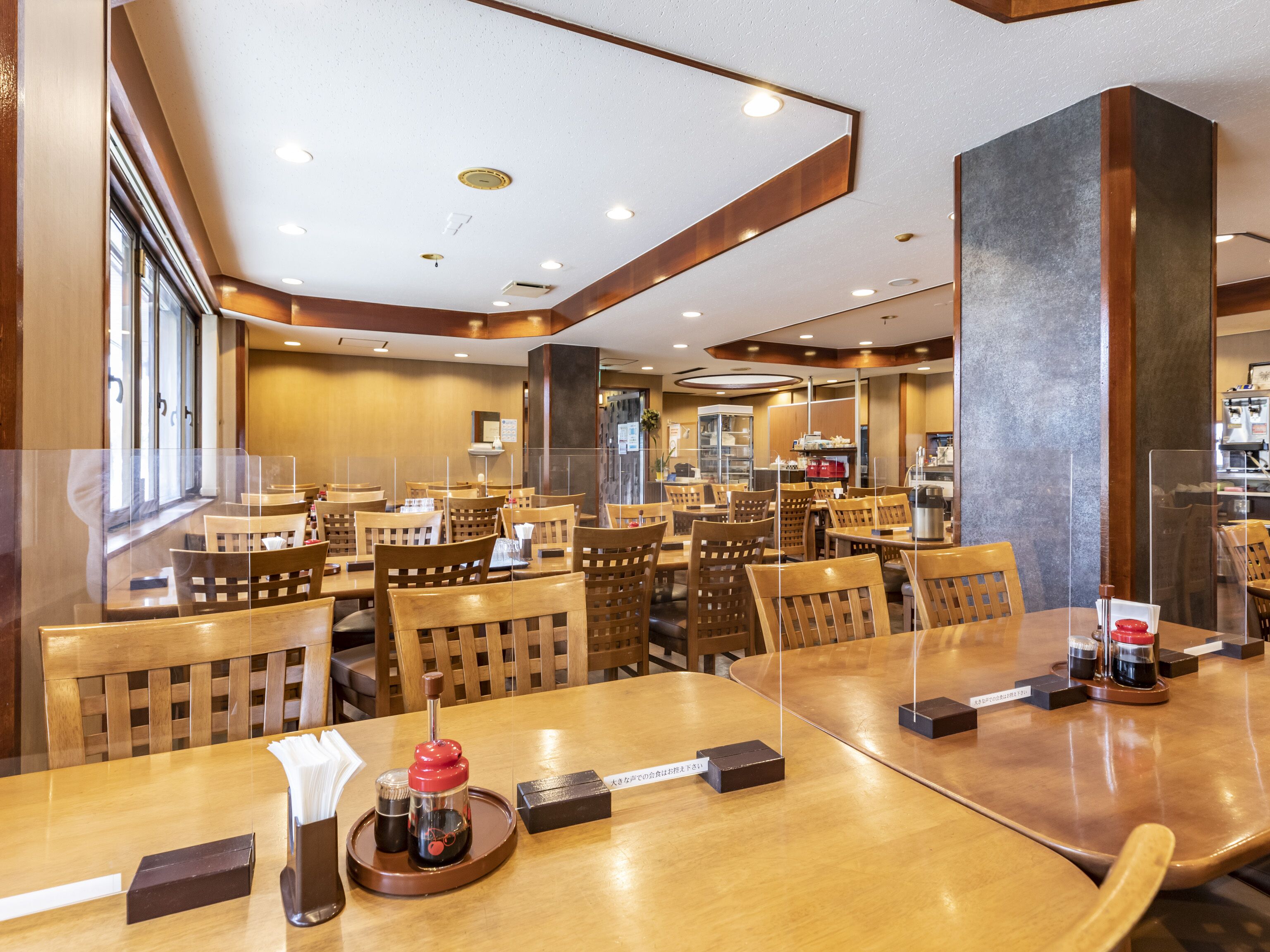 Um restaurante com mesas e cadeiras de madeira, uma máquina de café e um suporte para cardápio.