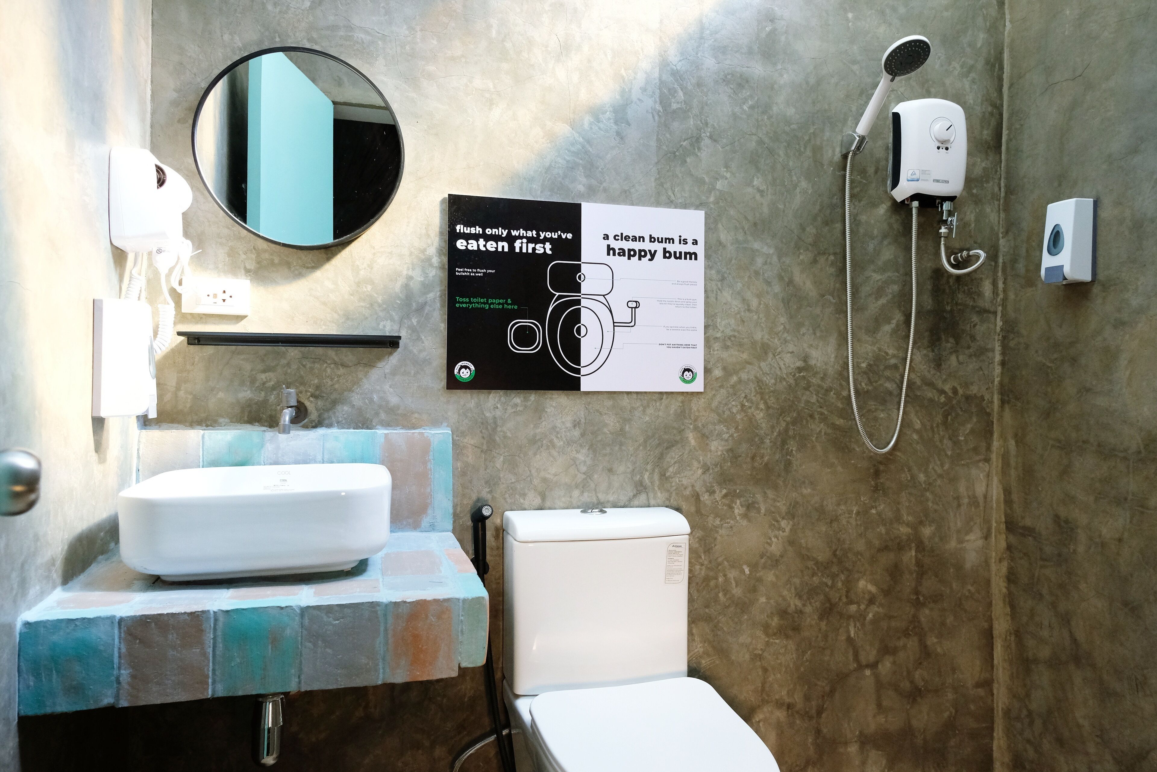 A bathroom with a white sink, a toilet, a mirror, and a shower. There's a sign on the wall with a message about cleanliness.