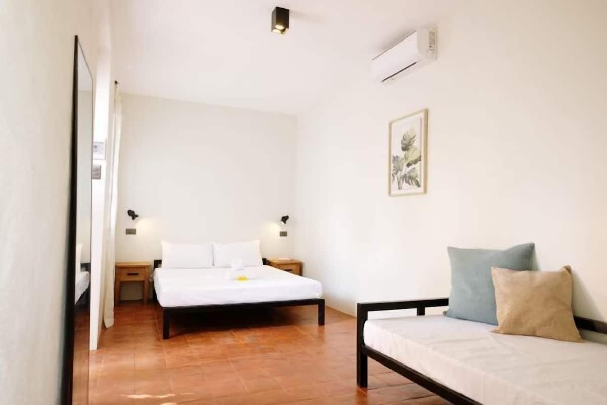 Une chambre à coucher comprenant un lit, des tables de chevet, une commode, un climatiseur fixé au mur et un tableau encadré.