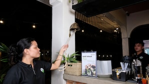 A bar area with a counter, a bell, a menu board, and a person serving. - Mad Monkey Dumaguete (Dumaguete)