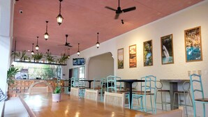 A restaurant with a long wooden table, teal chairs, hanging lights, ceiling fans, and framed pictures on the wall. - Mad Monkey Dumaguete (Dumaguete)