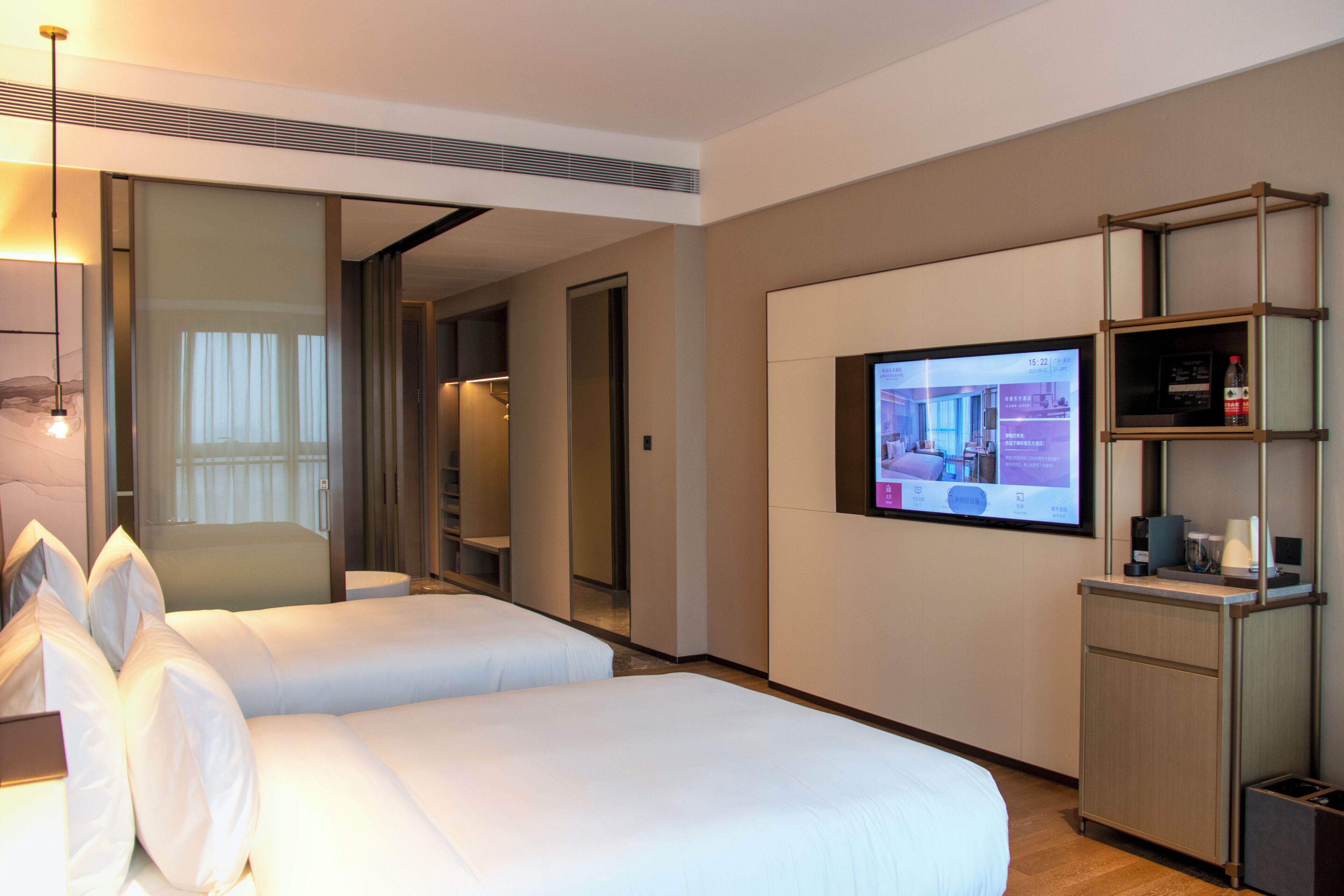 Ett hotellrum med två sängar, en tv på väggen, en minibar och en spegel.