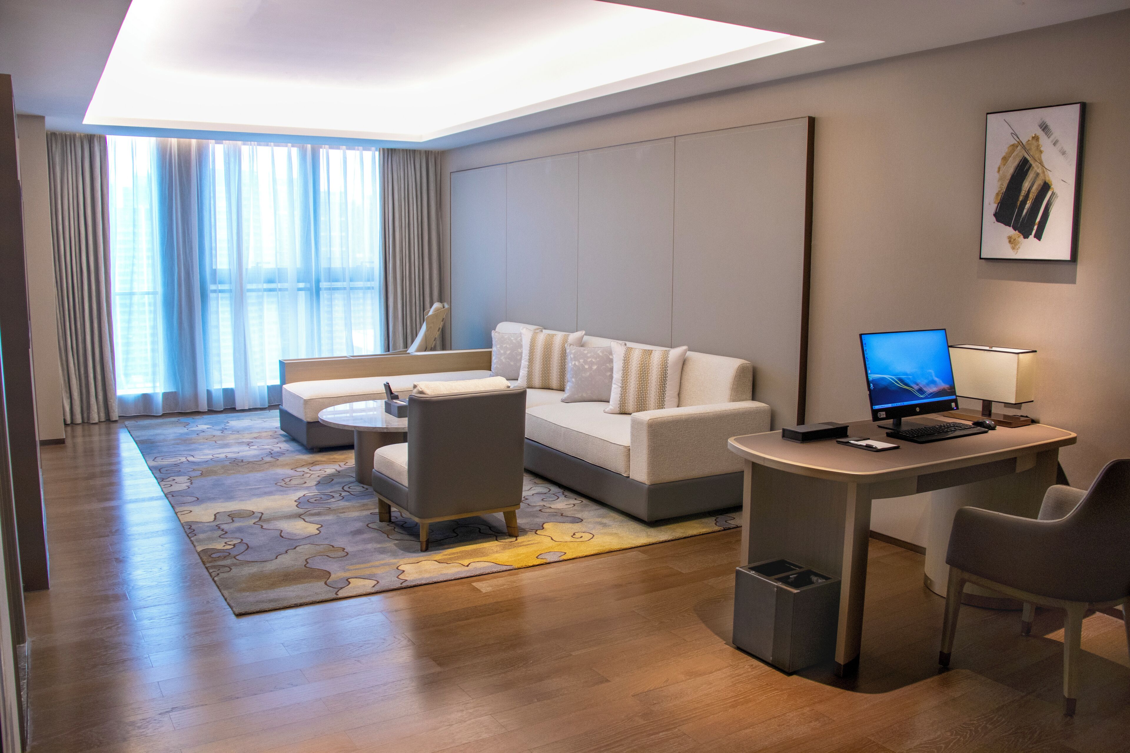 A modern hotel room with a sofa, a desk, a computer, and a small table.