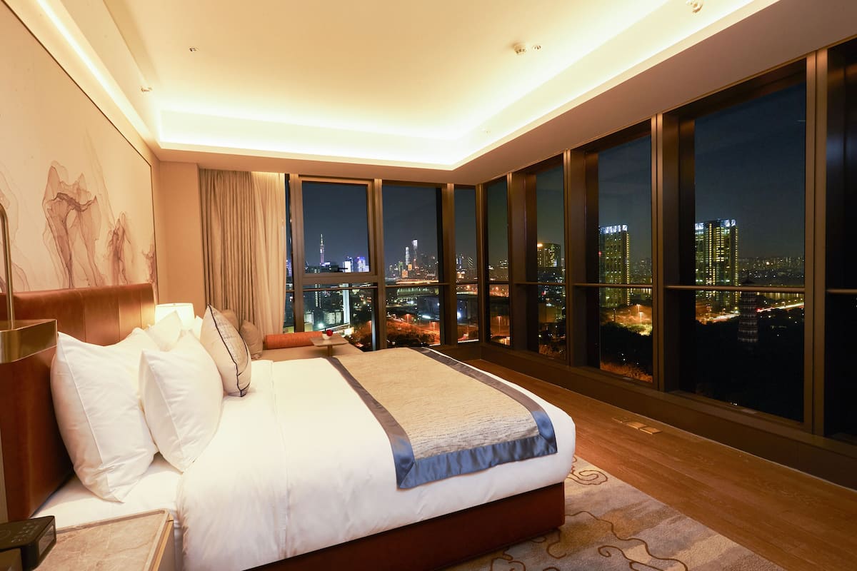 Een moderne hotelkamer met een groot bed, uitzicht op de stad en een stadsgezicht door de ramen.