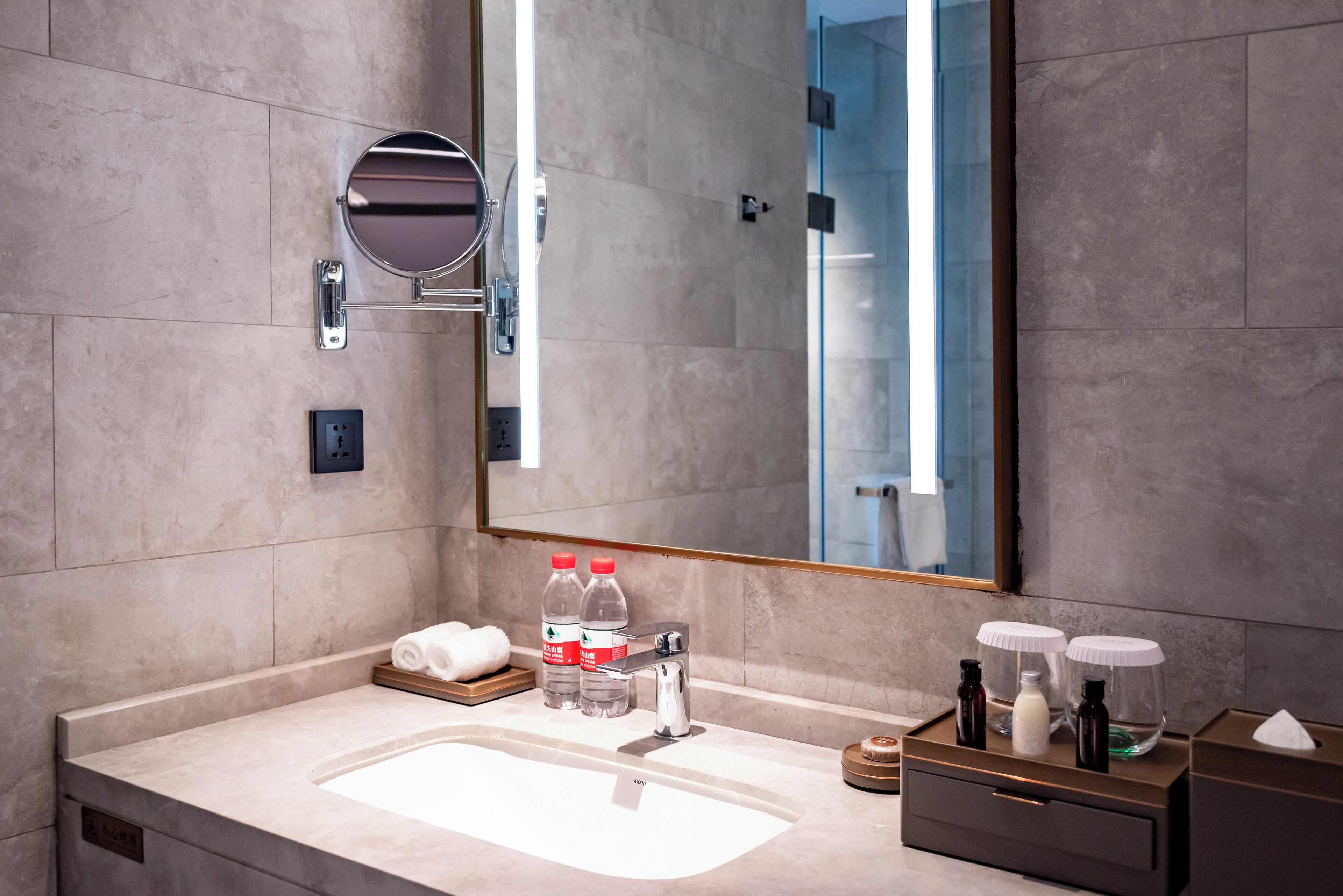 A modern bathroom with a large mirror, a sink, and a towel rack. There are two bottles of water and a bottle of lotion on the counter.