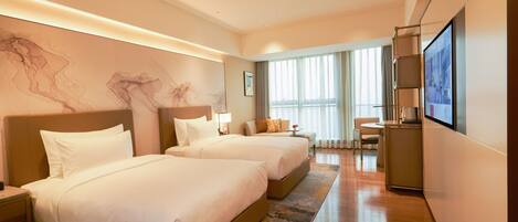 A hotel room with two beds, a desk, a chair, a TV, and a large window with curtains.