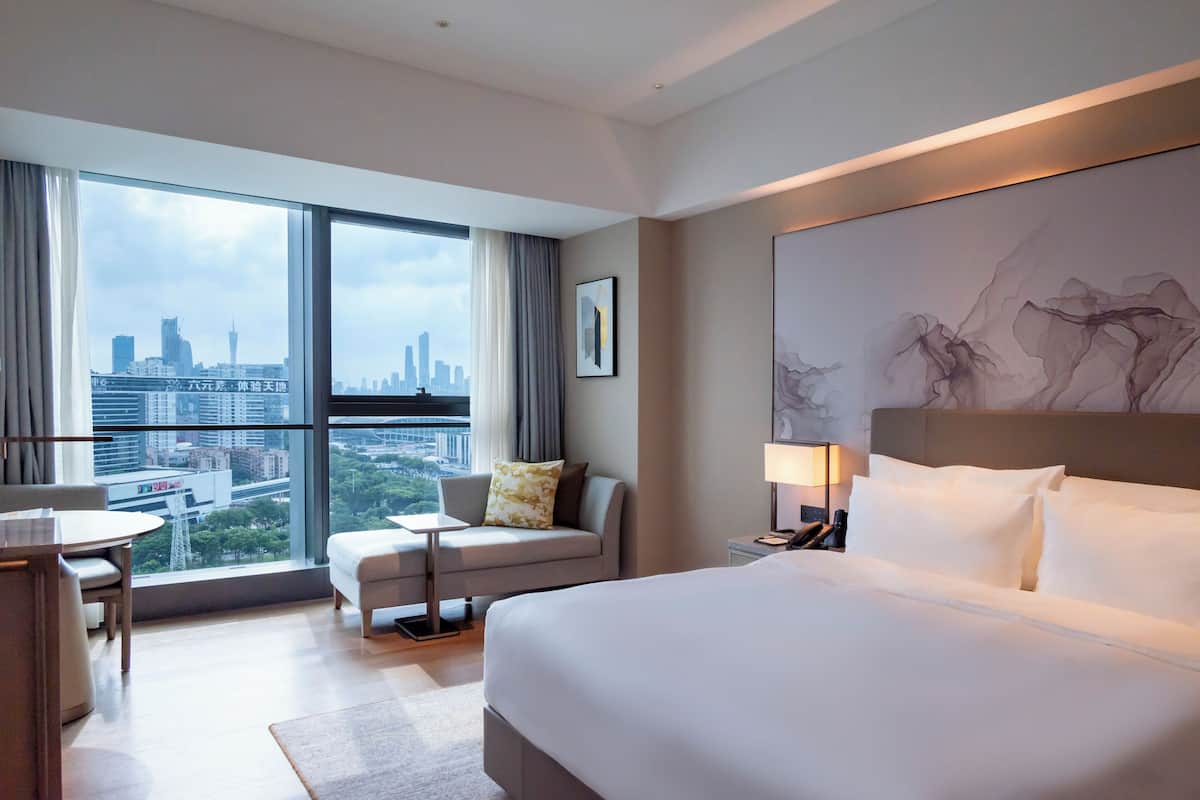 Een hotelkamer met een groot bed, een bank, een kleine tafel en een stoel. Er is een raam met uitzicht over de stad.