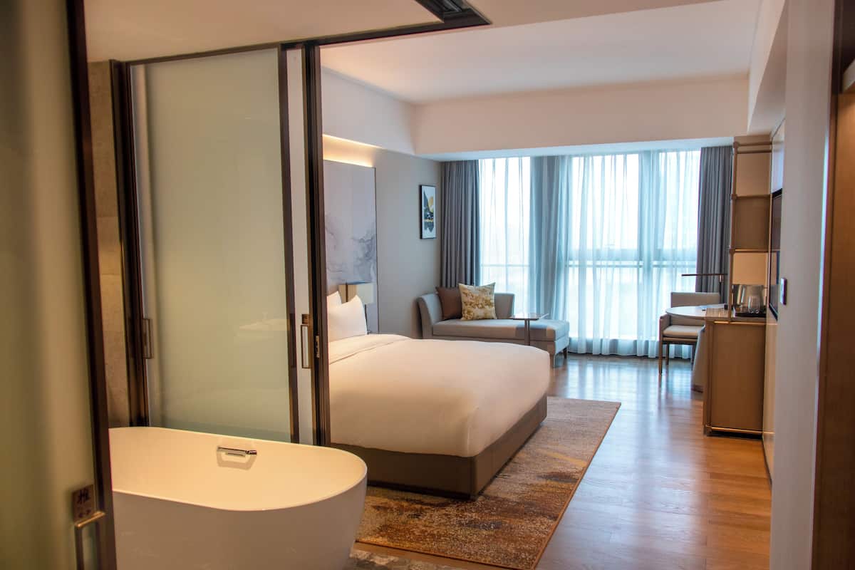 Een moderne hotelkamer met een groot bed, een zithoek met een bank en fauteuils, een kleine tafel en een kitchenette.