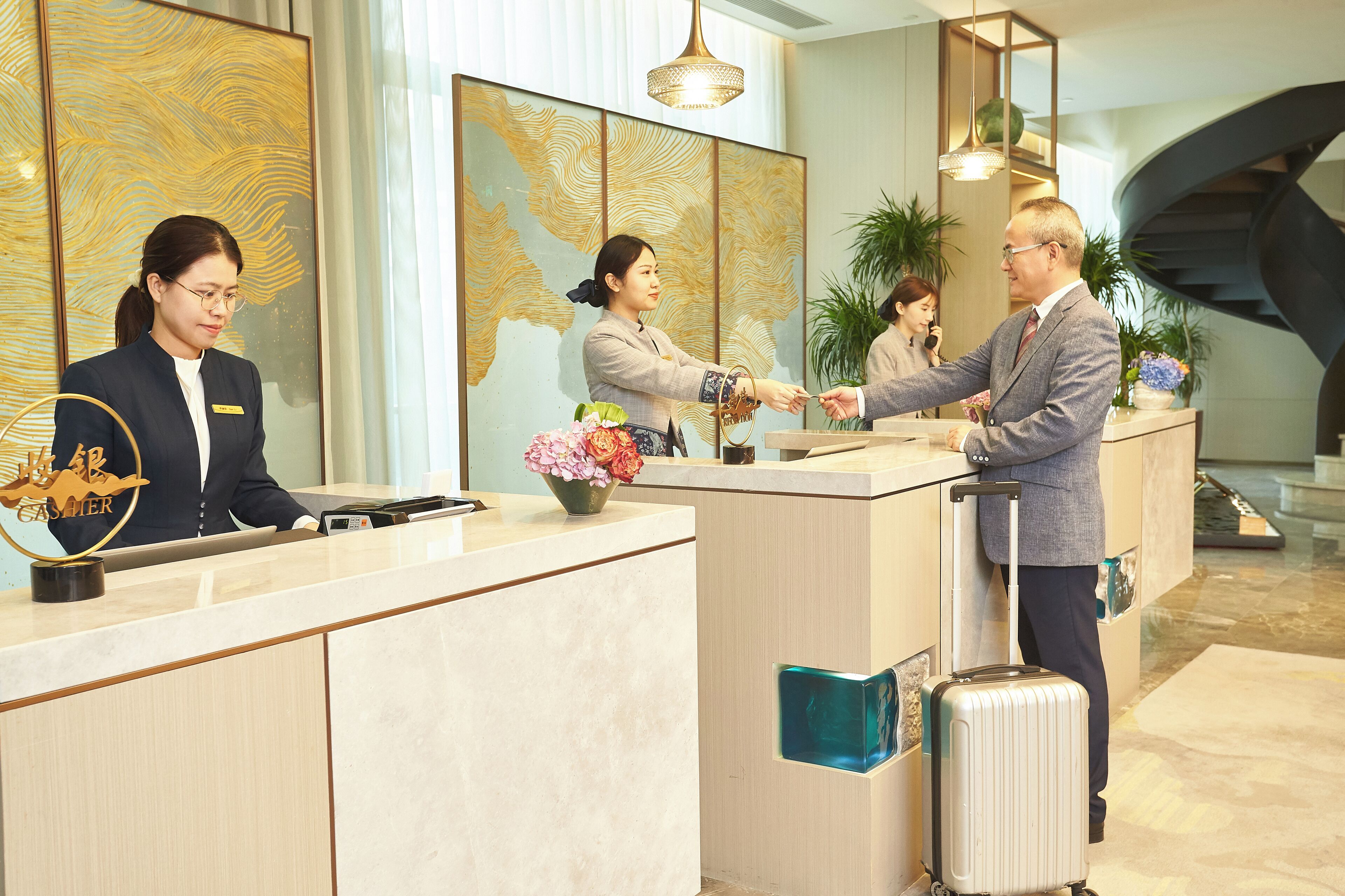 Mostrador de recepción de hotel con una recepcionista, un huésped y un hombre con una maleta.