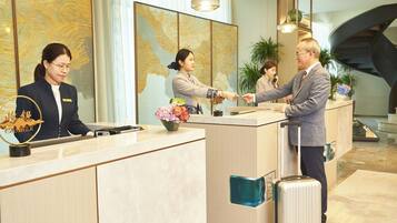 Mostrador de recepción de hotel con una recepcionista, un huésped y un hombre con una maleta.