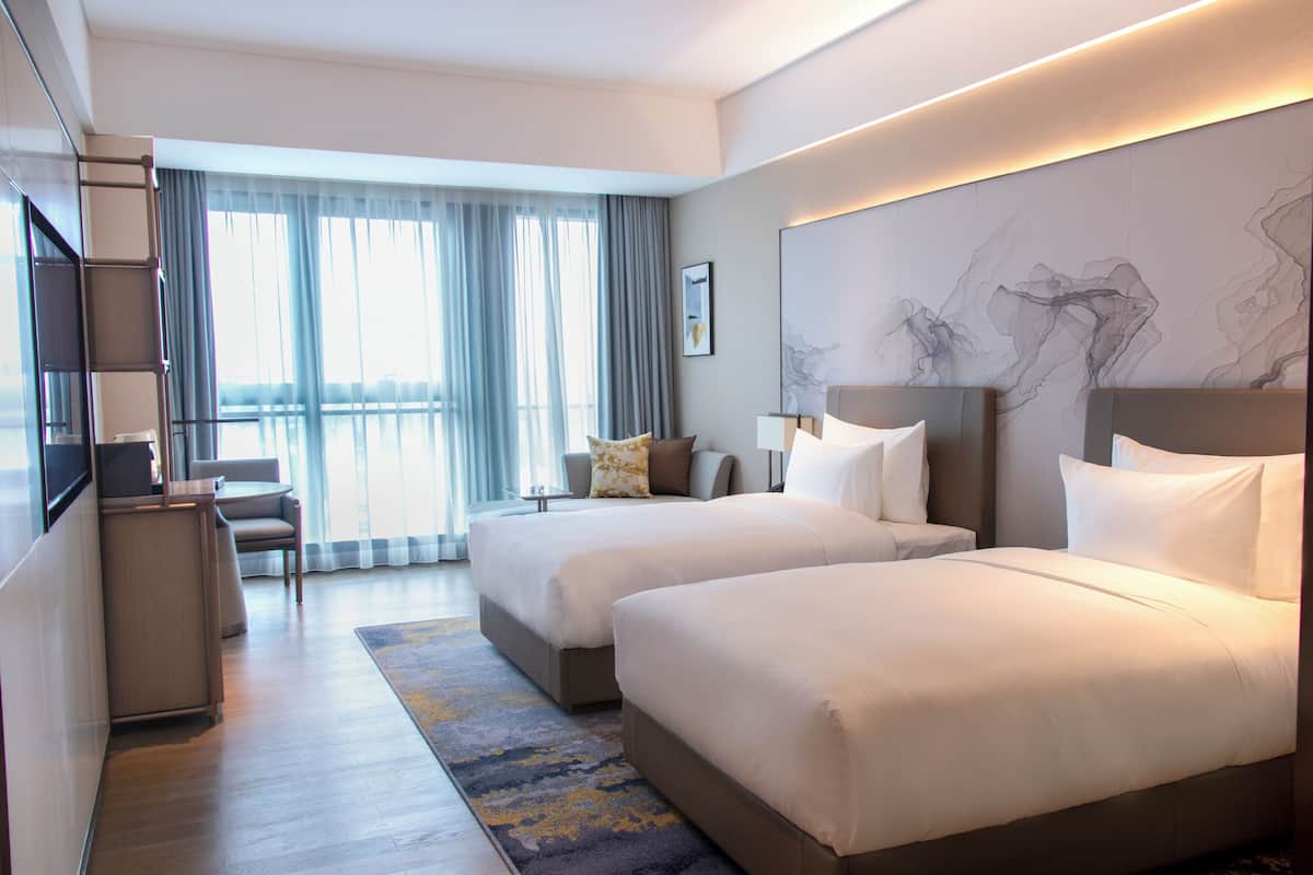 Een hotelkamer met twee bedden, een bureau, een stoel en een groot raam met gordijnen.