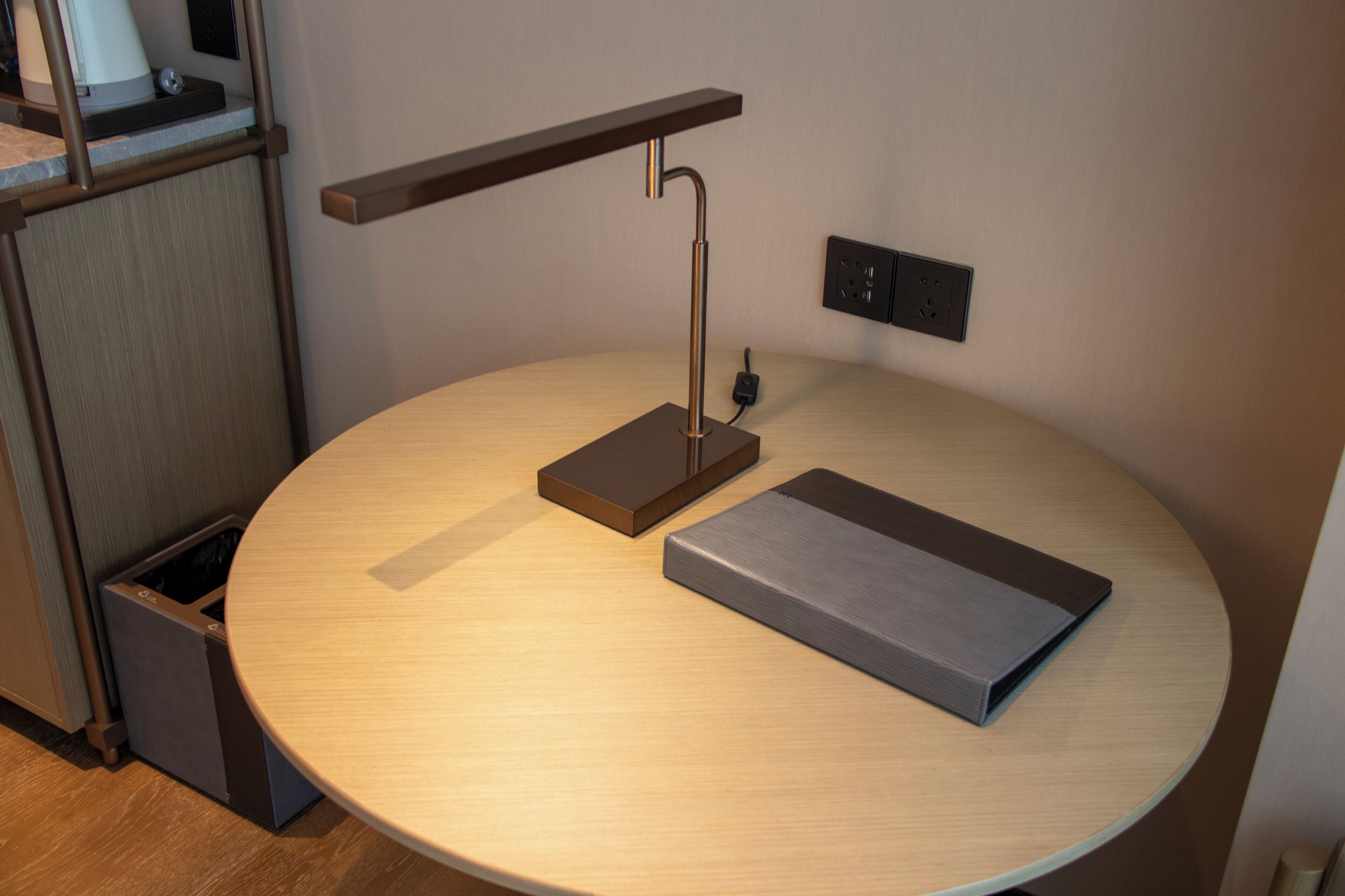 A round table with a modern lamp, a power outlet, and a trash bin.