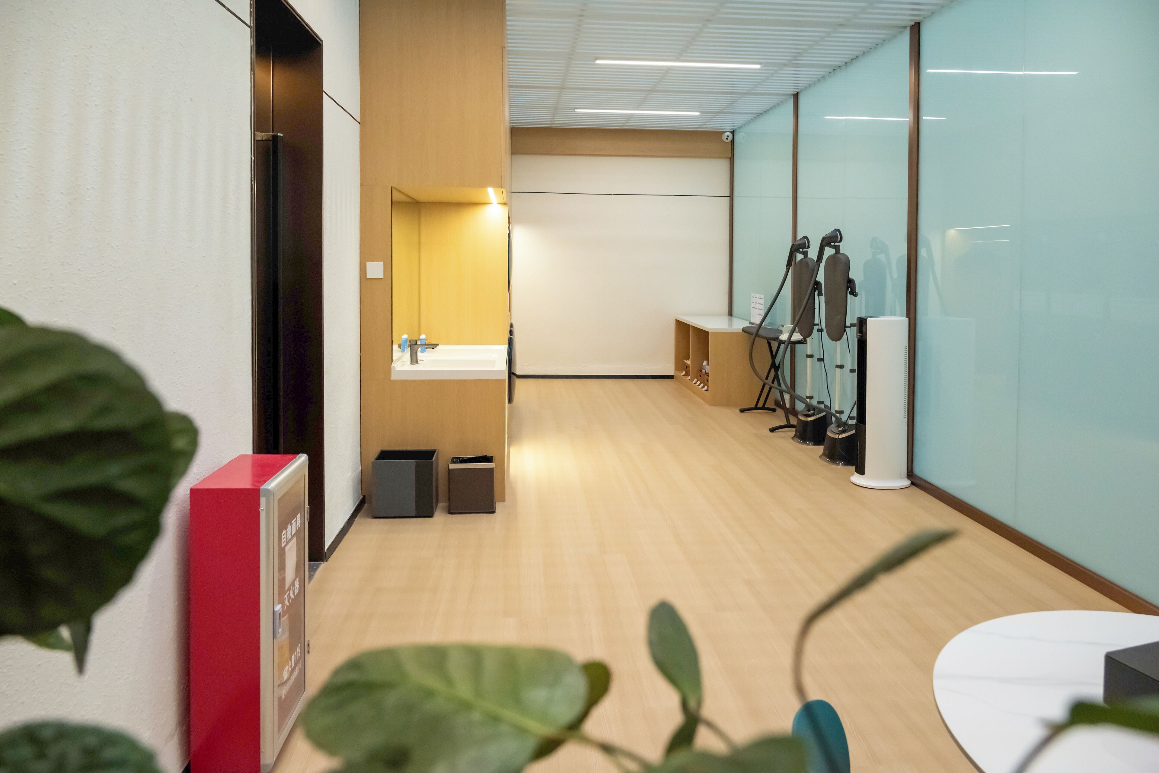 A modern office space with a wooden floor, a white reception desk, a mirror, and exercise equipment.