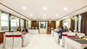 Ein Konferenzraum mit weißen Tischen und Stühlen, großen Fenstern und Vorhängen.