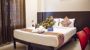 Ein Hotelzimmer mit einem ordentlich bezogenen Bett, einer Blumenvase und einem roten Sessel.