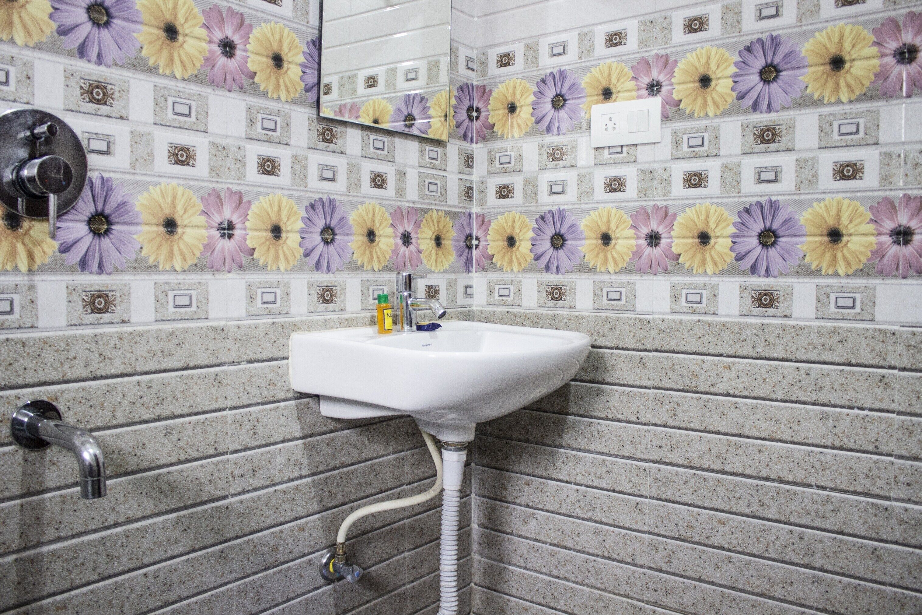 Une salle de bain avec un lavabo, un miroir et des murs carrelés ornés d’un motif floral.