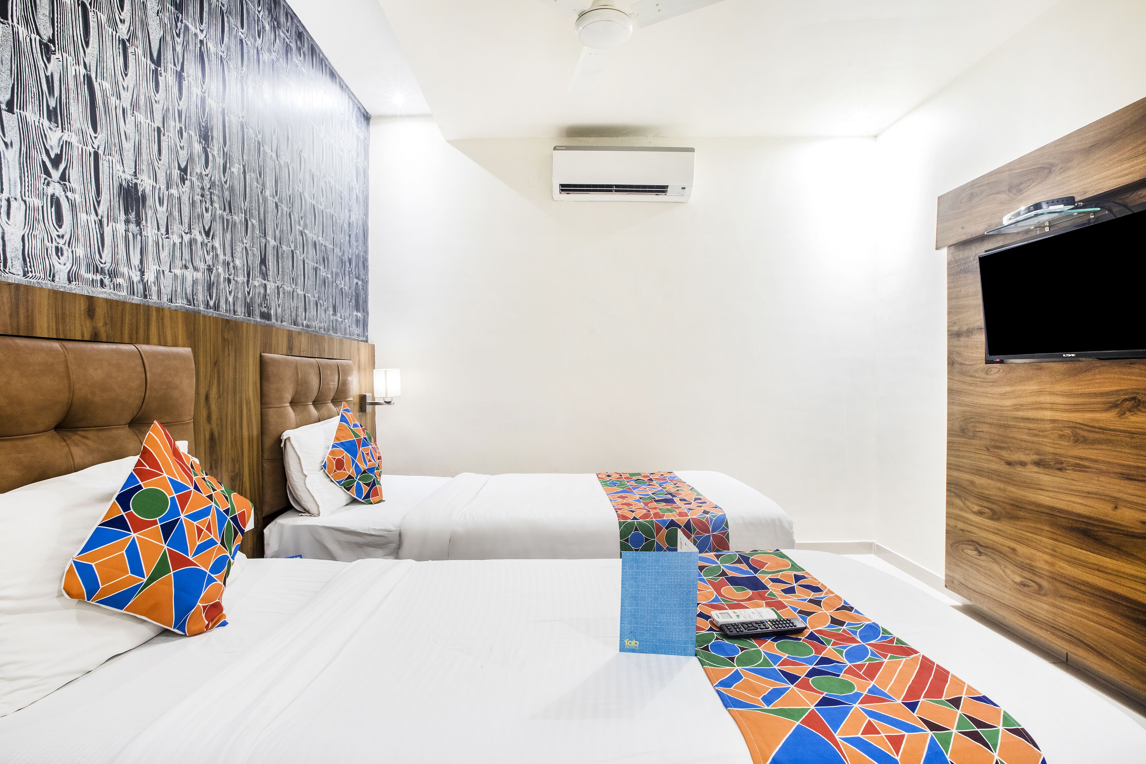 A hotel room with two beds, a wooden headboard, a flat-screen TV, and a patterned bed runner.