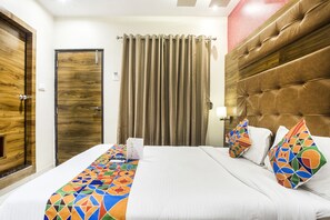 A hotel room with a large bed, a wooden door, a curtain, and a headboard. - Fabhotel Amour (Mumbai)