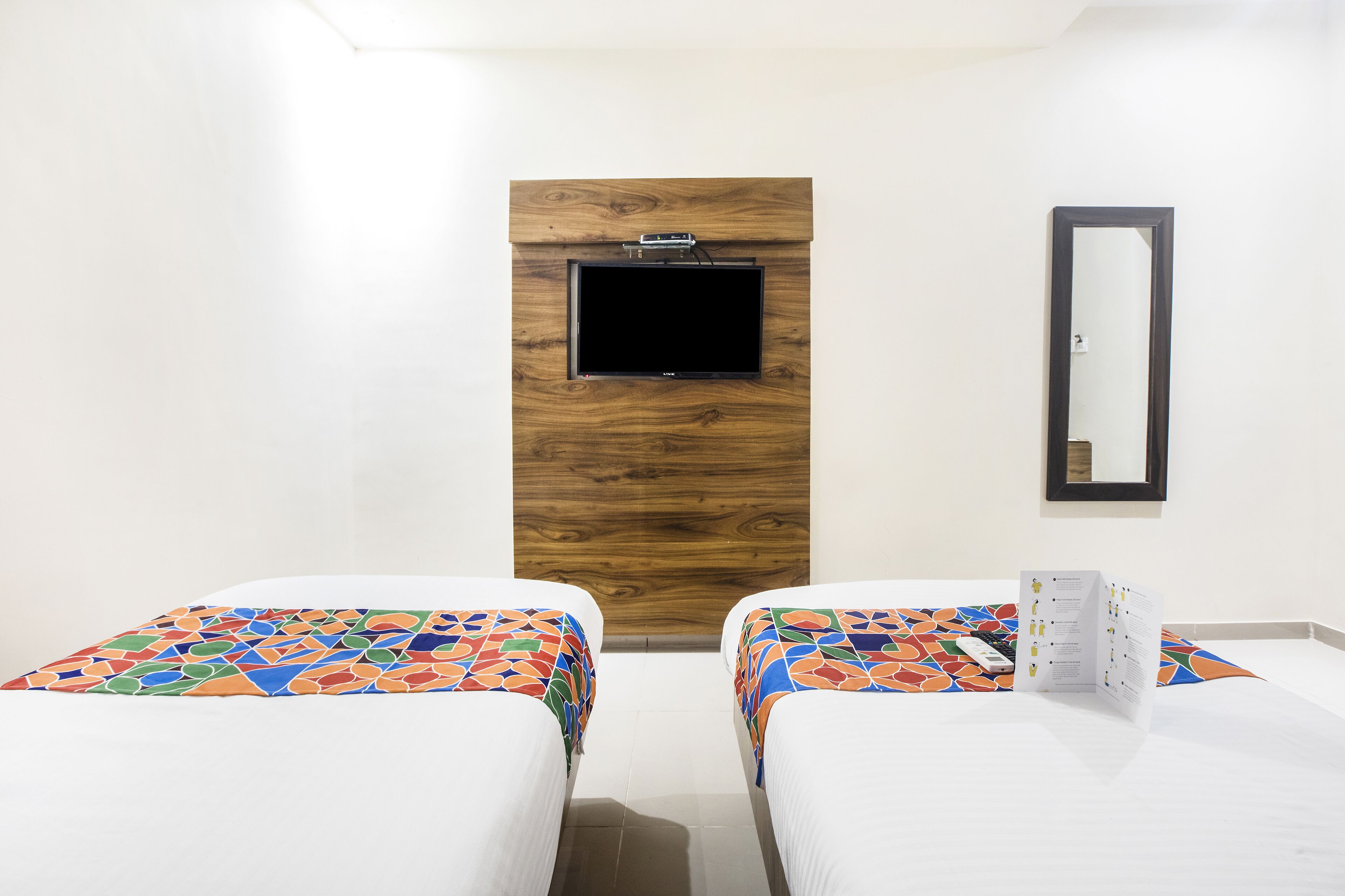 A hotel room with two beds, a wooden accent wall, a mounted TV, and a mirror.