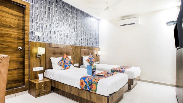 A hotel room with two beds, wooden headboard, a patterned wall, and a ceiling fan. - Fabhotel Amour (Mumbai)