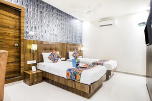 Habitación de hotel con dos camas, cabecero de madera, pared con diseño y ventilador de techo.