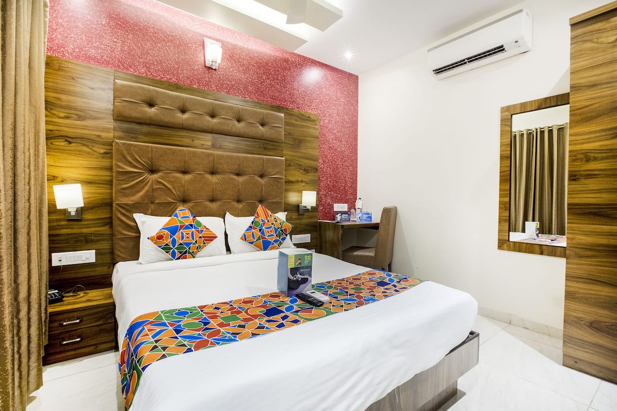 A hotel room with a large bed, a wooden headboard, a red accent wall, and a mirror.