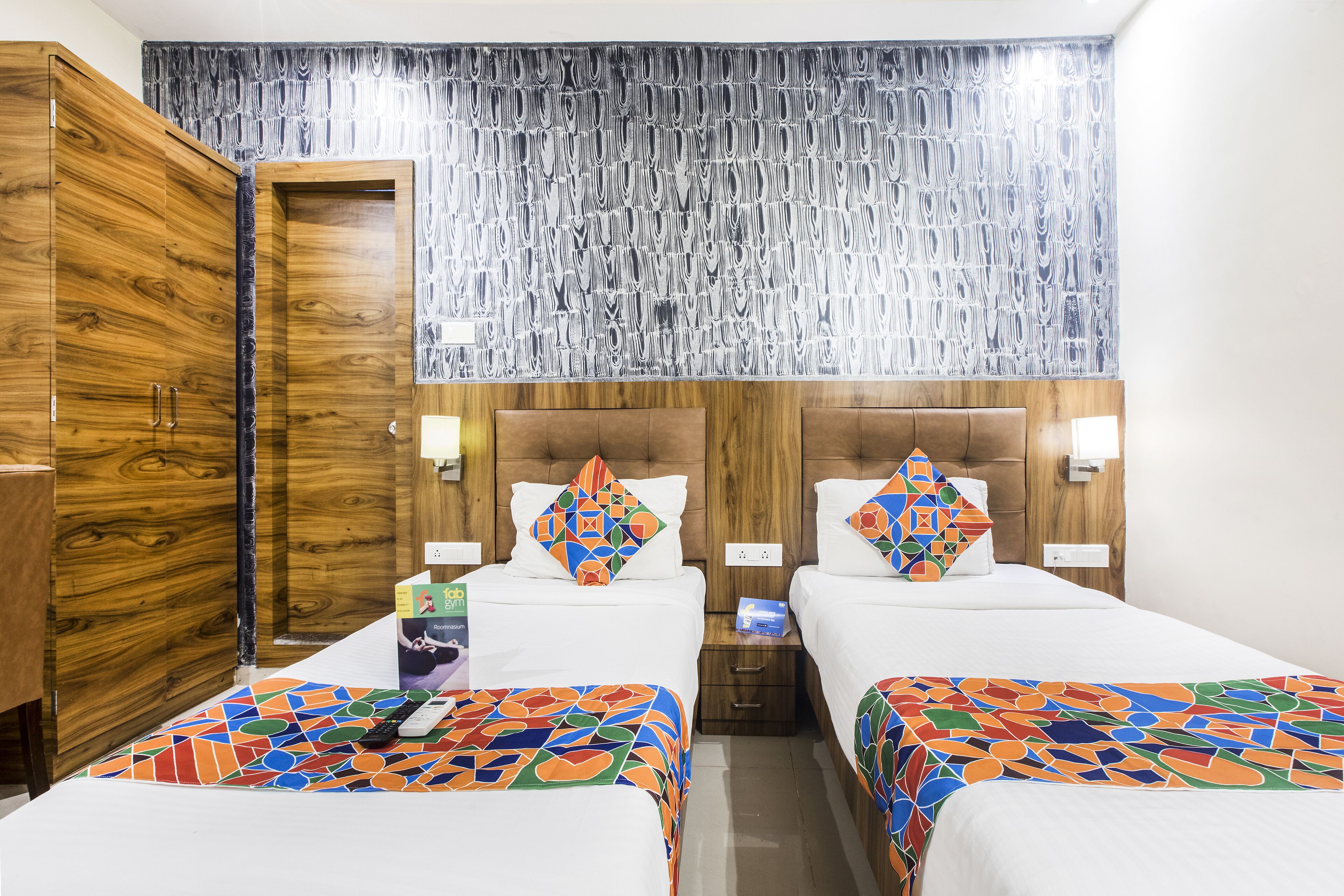 A hotel room with two beds, wooden wardrobe, and a patterned curtain.